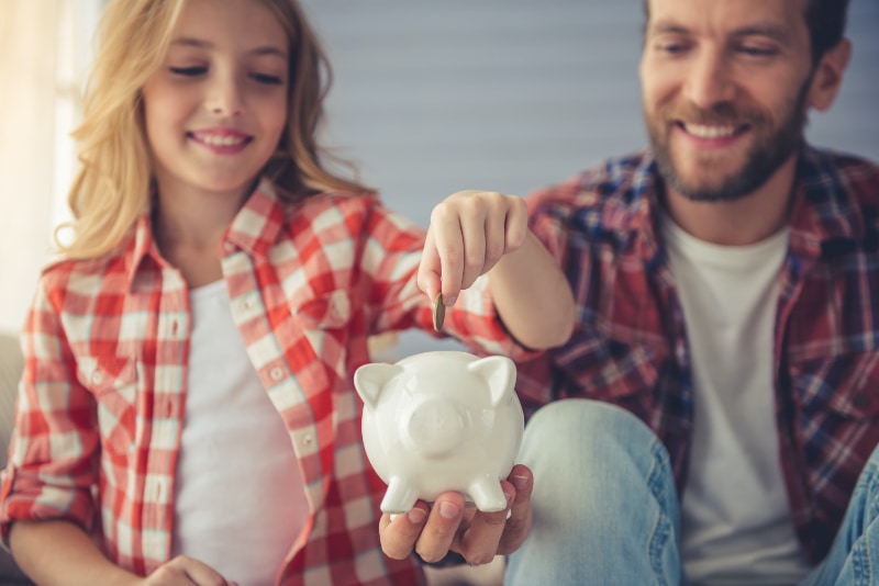 Girl putting money into piggy bank for education savings.