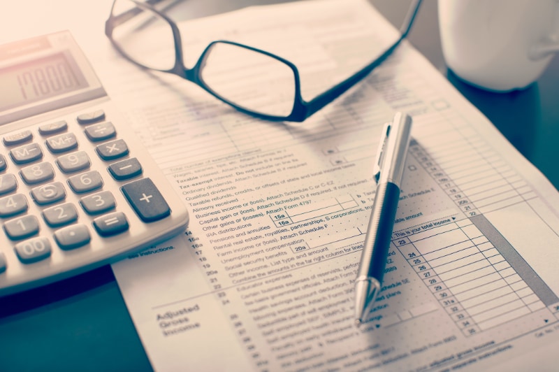 Tax documents sitting on desk with calculator, glasses, and a pen.